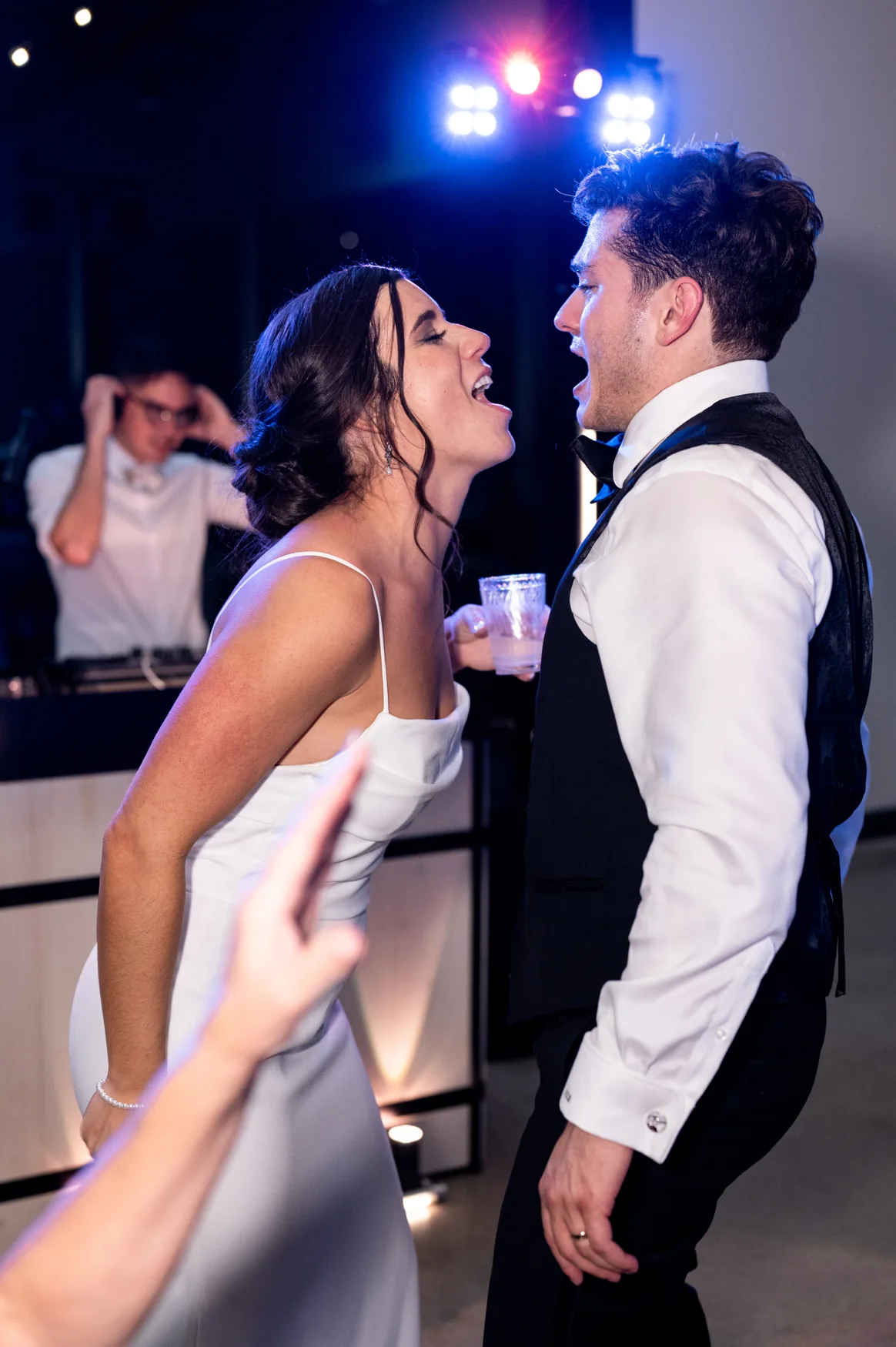A bride and groom singing together on a packed wedding dance floor.