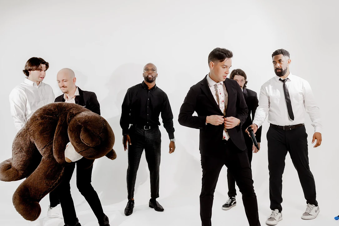 The Upchurch DJ crew in suits at the white studio shoot, one carrying a giant teddy bear.