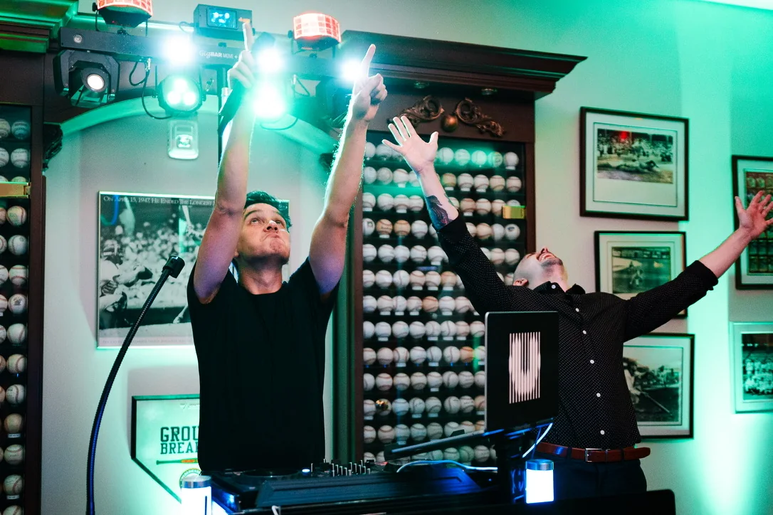 An Upchurch DJ raising both hands behind the booth as the crowd dances.