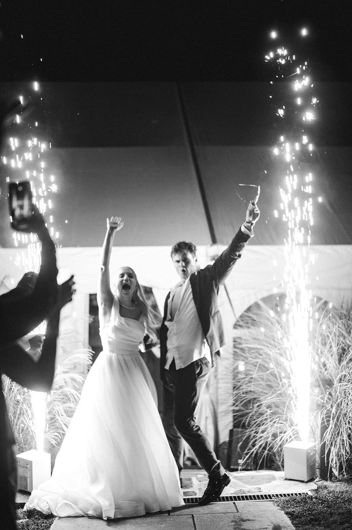The bride and groom cheering at their sparkler send-off between two fountains of cold sparks.